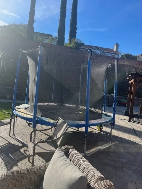 Backyard with a trampoline, patio furniture, and a clear blue sky.