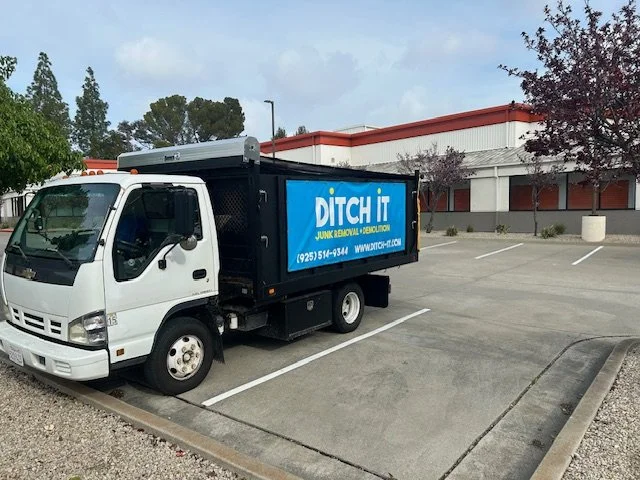Trash removal truck parked in an empty parking lot near a commercial building.