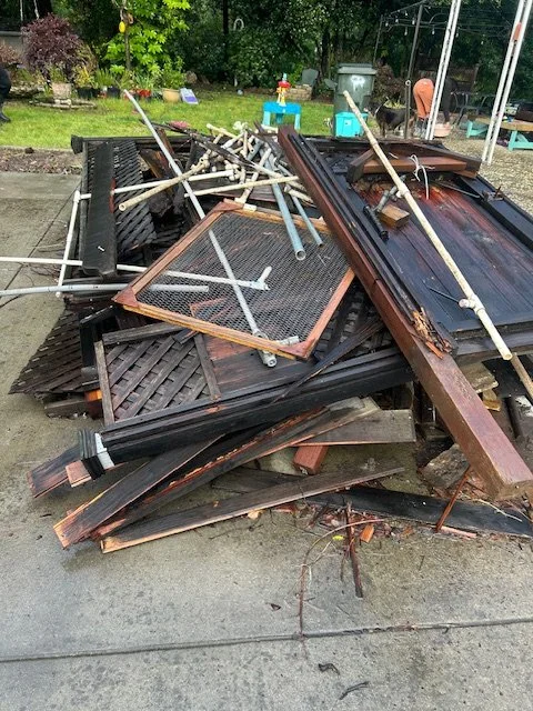 Piles of broken and discarded outdoor furniture and wooden structures on concrete, with equipment and trees in the background in Pleasant Hill, CA