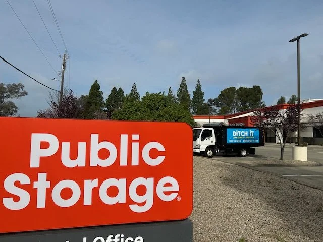 Public Storage facility with a large sign in foreground; a truck with "Ditch It" advertisement parked nearby.