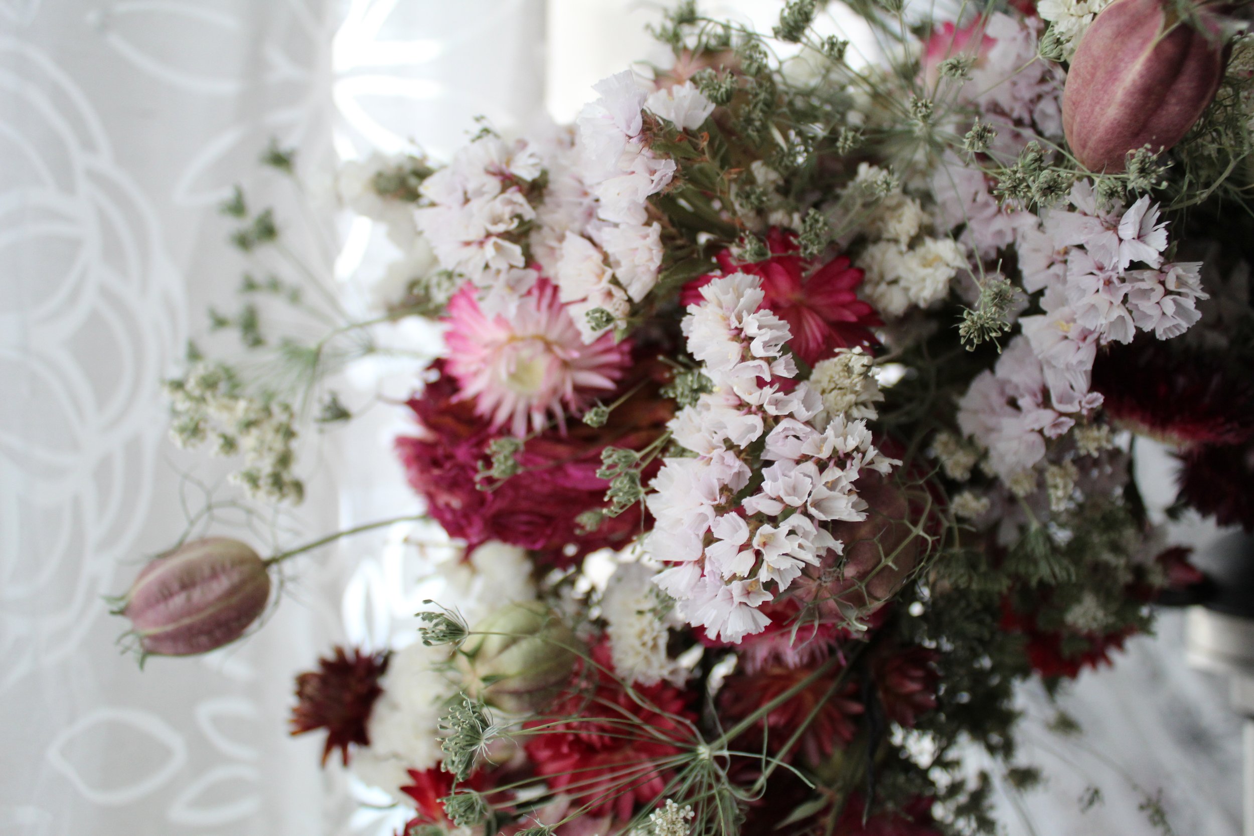 Close up of a February wreath featuring dried strawflower, laceflower, statice, and nigella seed pods.