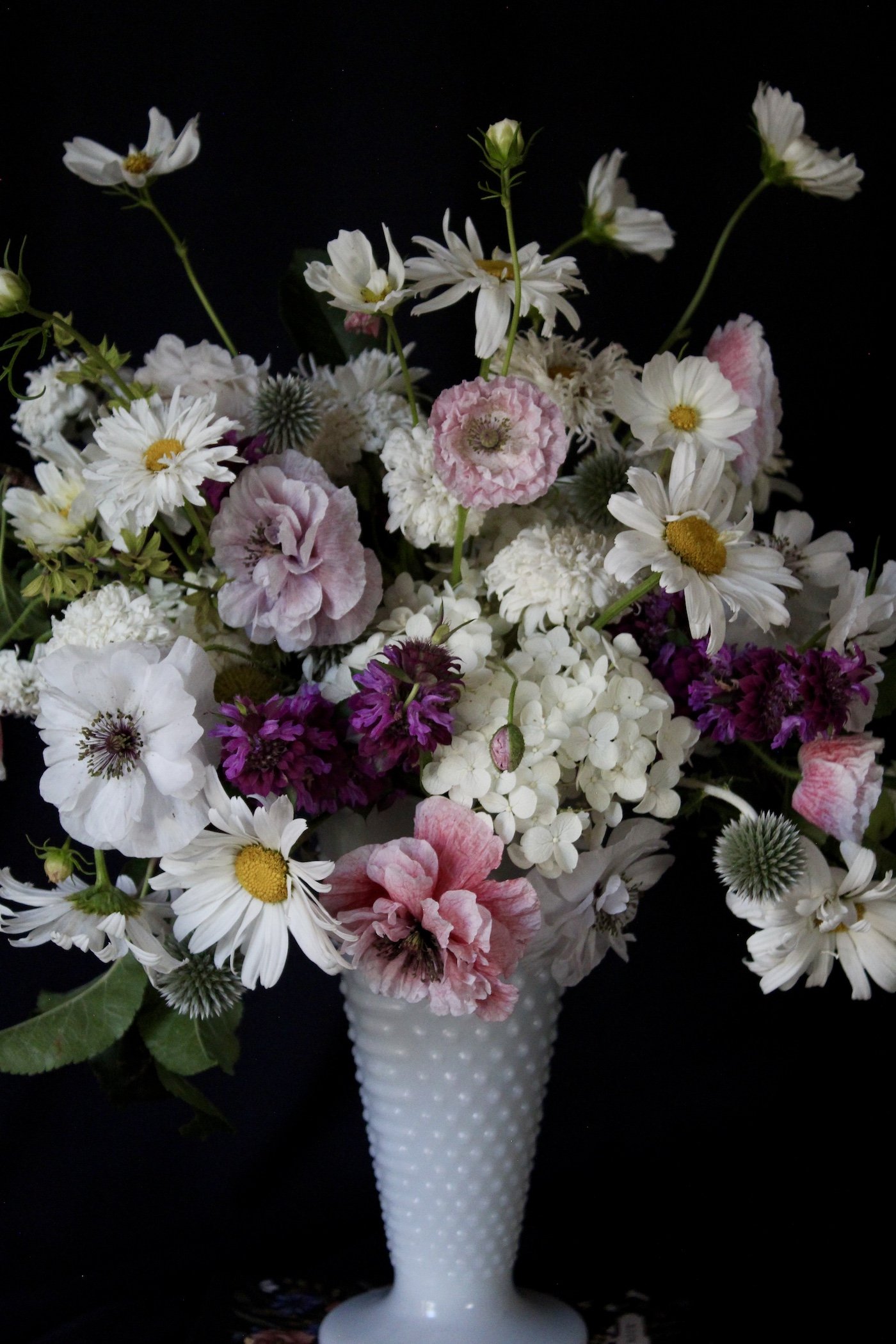 A soft summer arrangement of shirley poppies, cosmos, hydrangeas, and globe thistle.