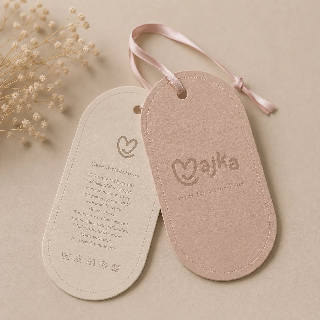 Elegant clothing tag and packaging design for Majka motherhood brand featuring soft pastel tones, embossed logo details and premium paper textures.