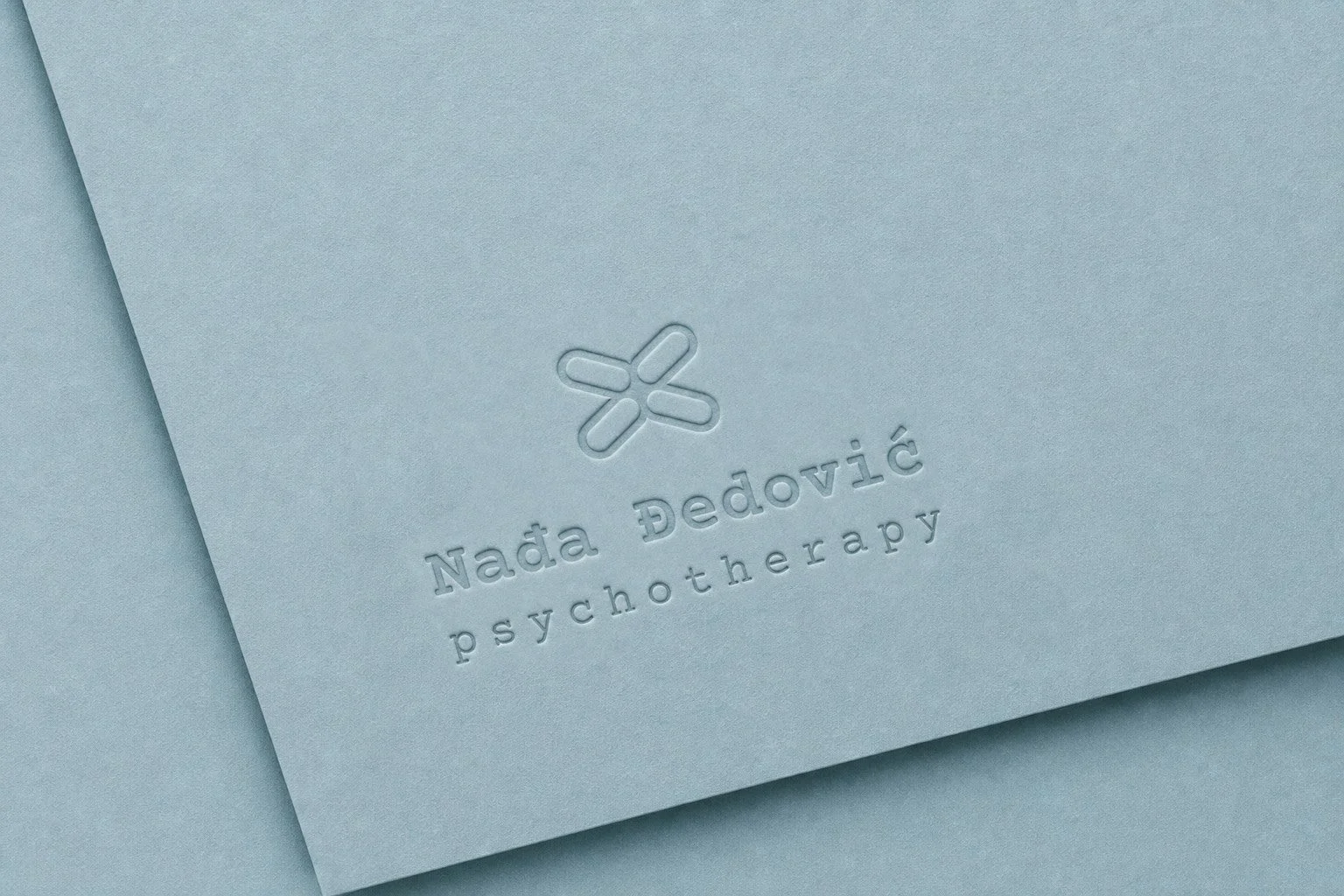 Embossed logo mockup on textured soft blue paper for Nađa Đedović Psychotherapy brand identity