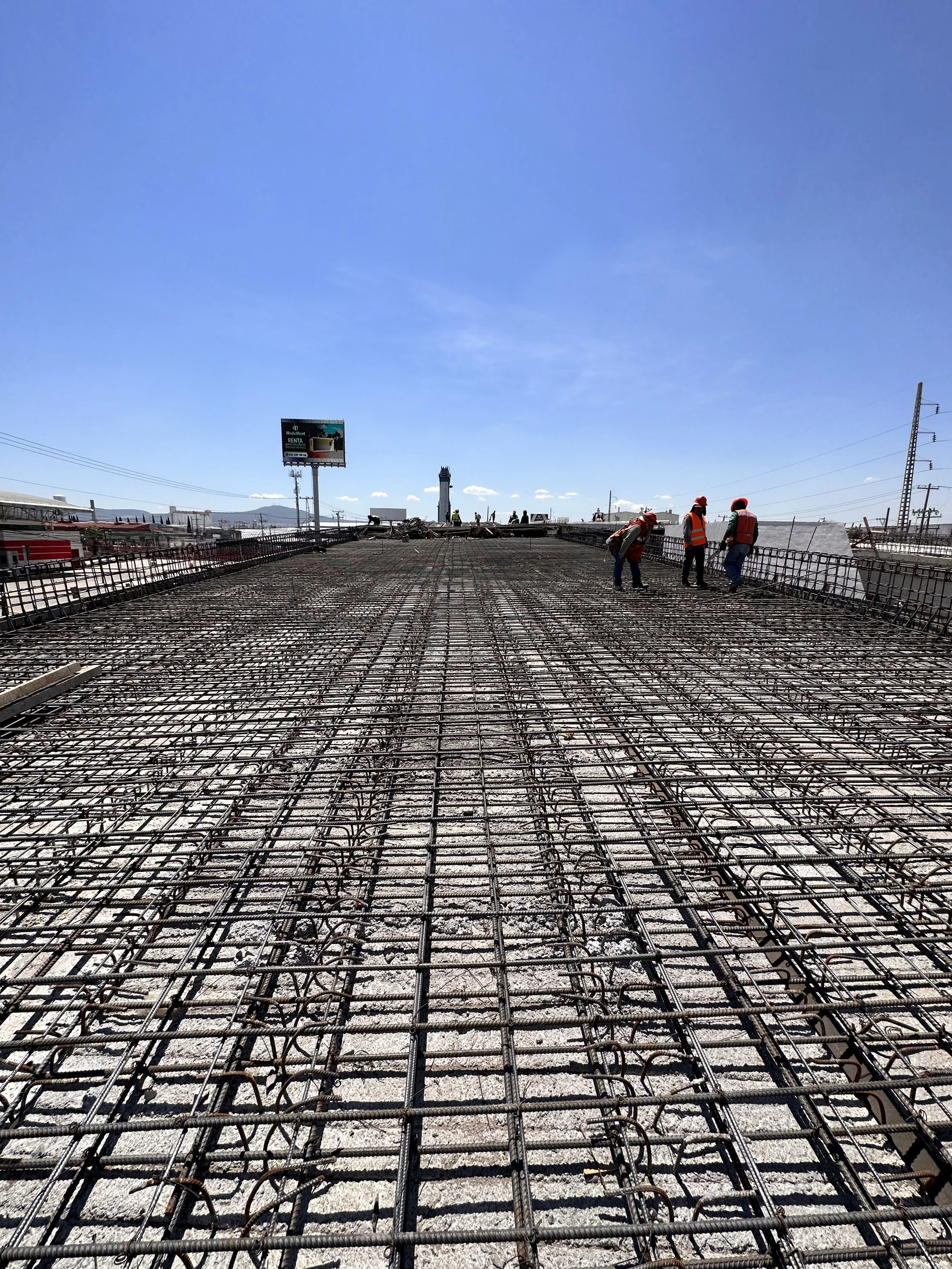 Trabajadores en una construcción de puente con estructura de acero y cables de acero en un día soleado.