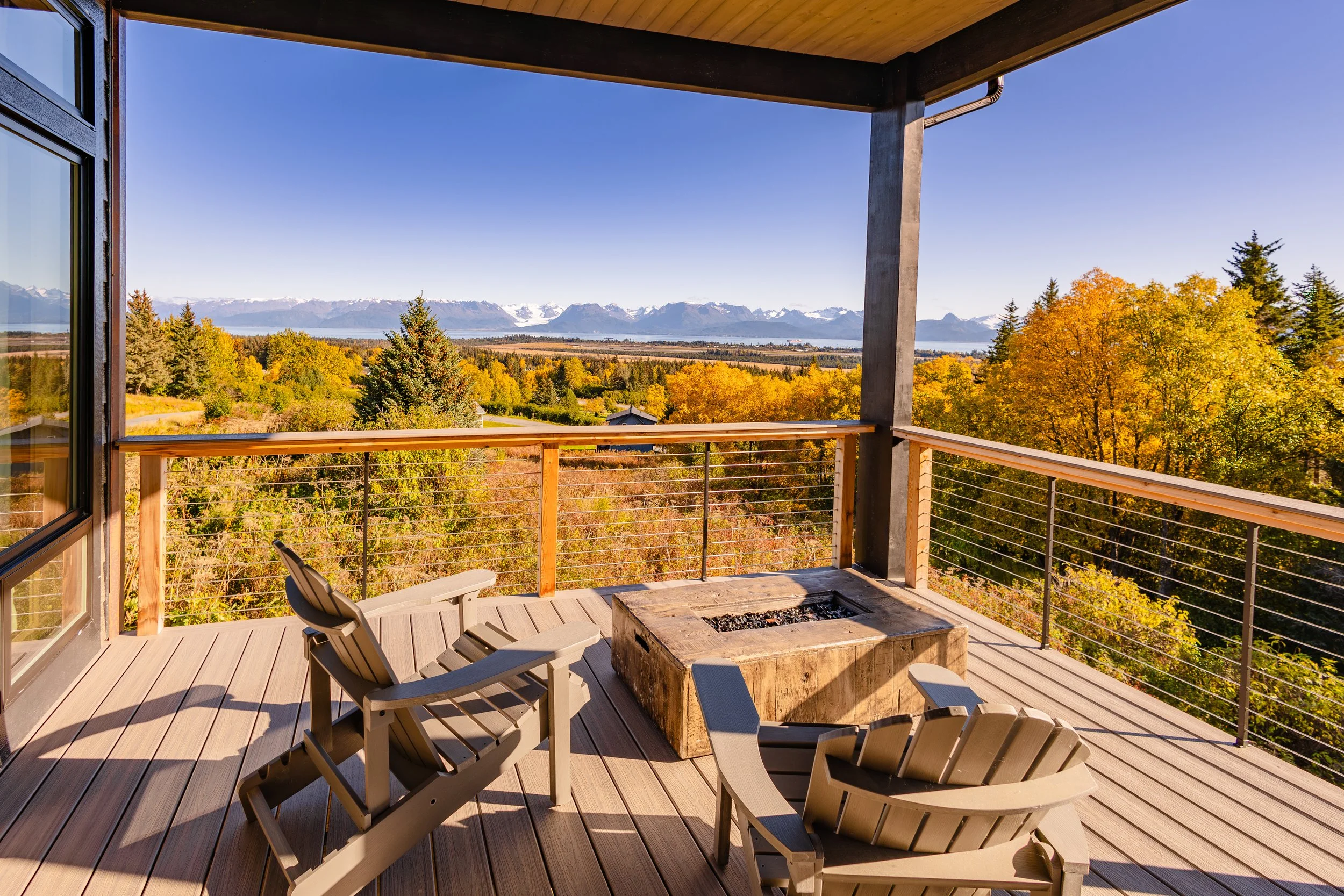 Deck with Adirondack chairs and fire pit, overlooking autumn trees and distant mountains.