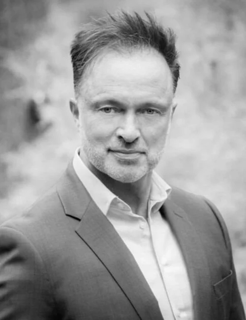 Black and white portrait of a man in a suit, posing outdoors with a neutral expression.