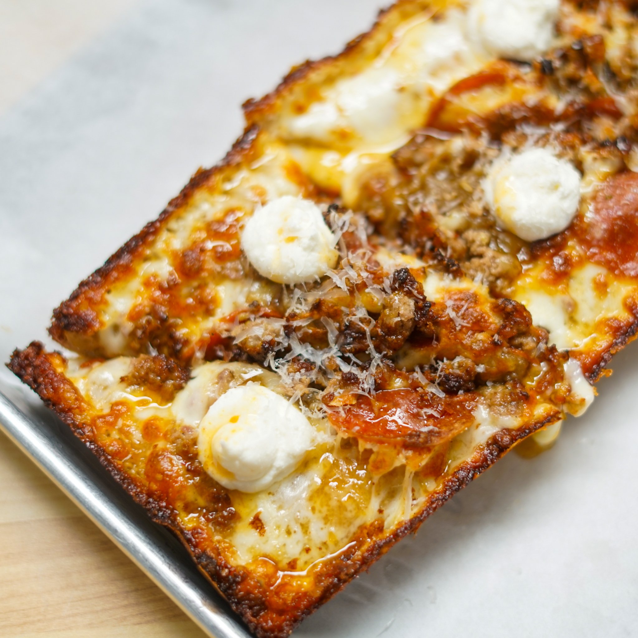 A rectangular pizza with cheese, sausage, dollops of ricotta cheese, and grated cheese crust on a baking sheet.