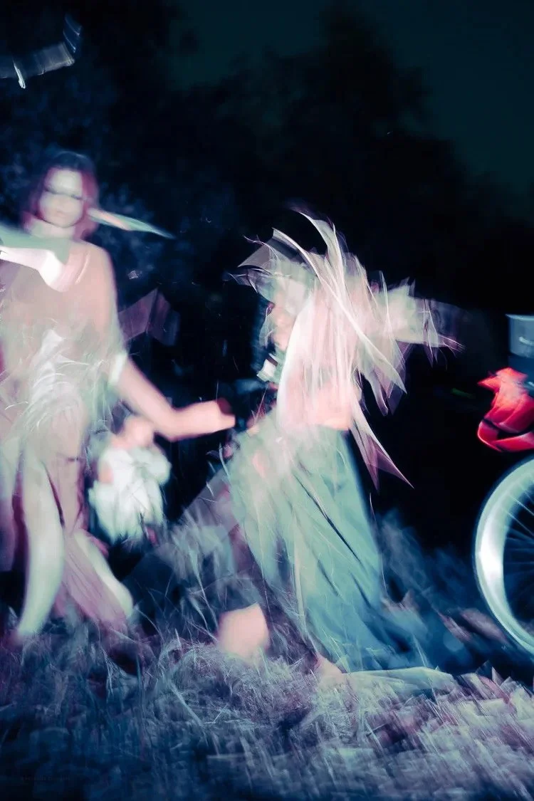 A woman with glasses holding a child, with a person wearing a bright orange shirt nearby, in a dark environment with motion blur and lights.