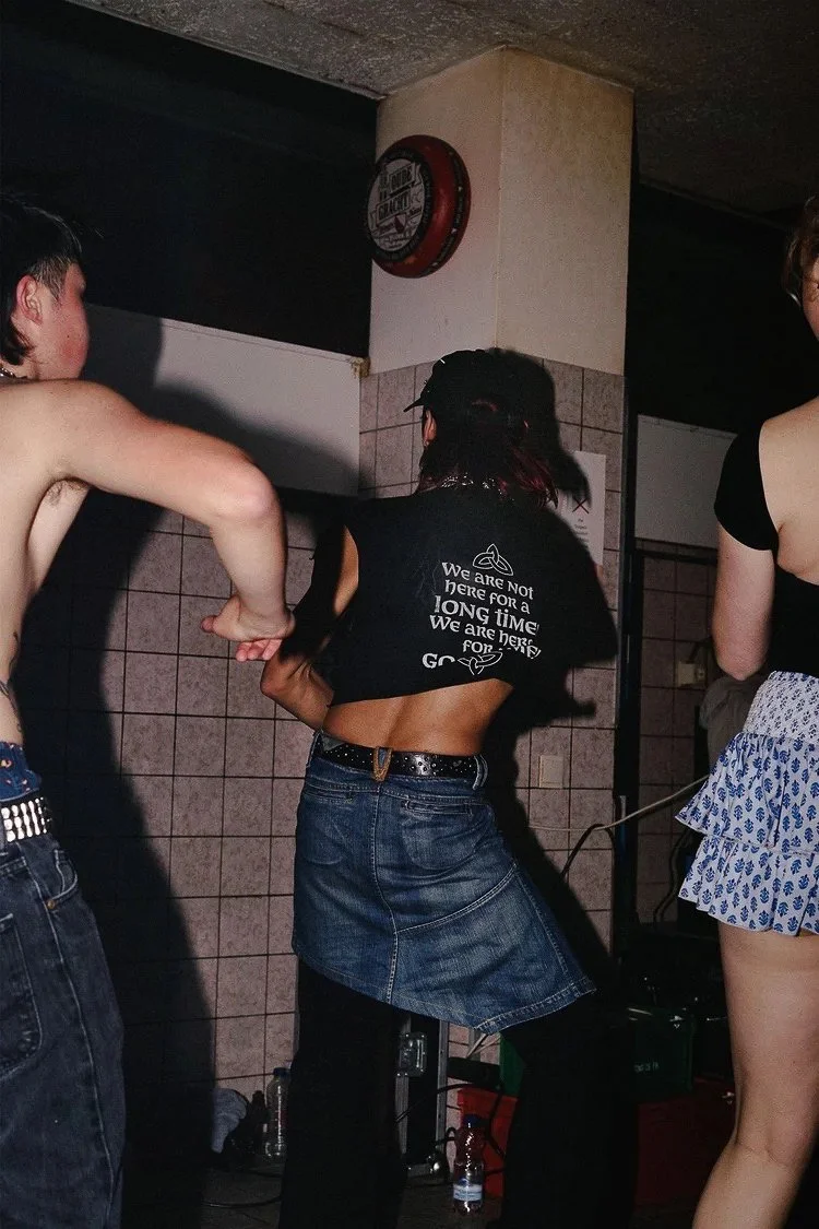 Group of people dancing in a dimly lit room with tiled walls and a clock on the wall.