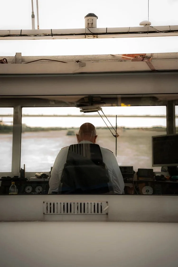 Person with a bald head sitting in a control tower at an airport, looking out at the runway and airplanes.