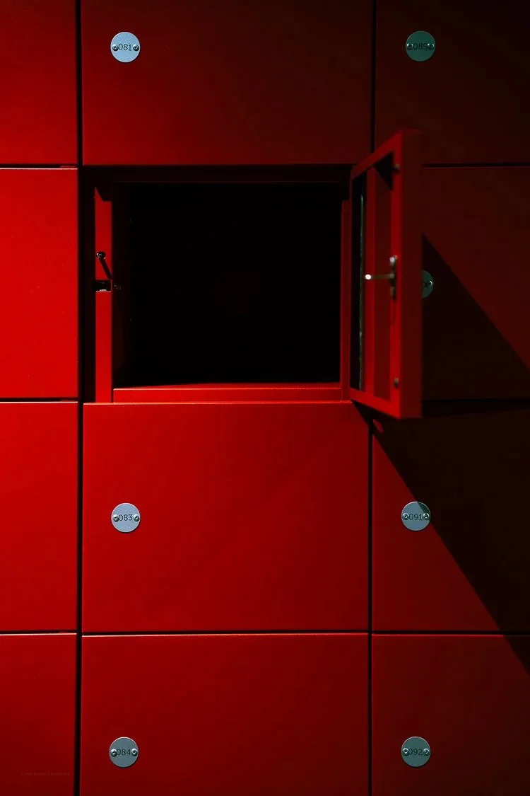 Red lockers with one open locker showing an empty dark interior, and numbered circular tags on the lockers.