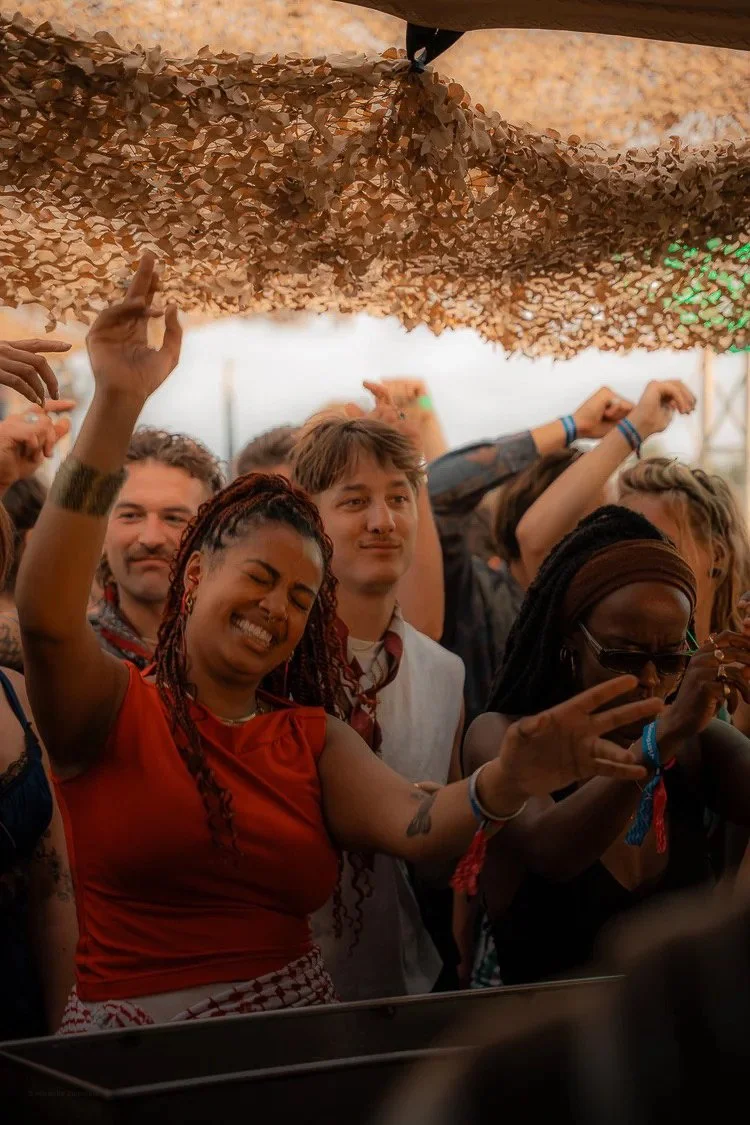 A crowd of people at a music festival dancing and enjoying themselves under a camouflage net canopy.