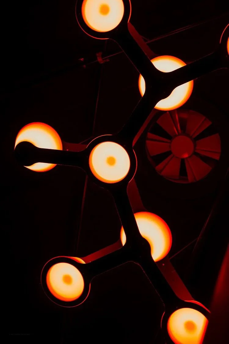 Close-up of a modern chandelier with multiple round, glowing orange lights connected by black structural elements against a dark background.