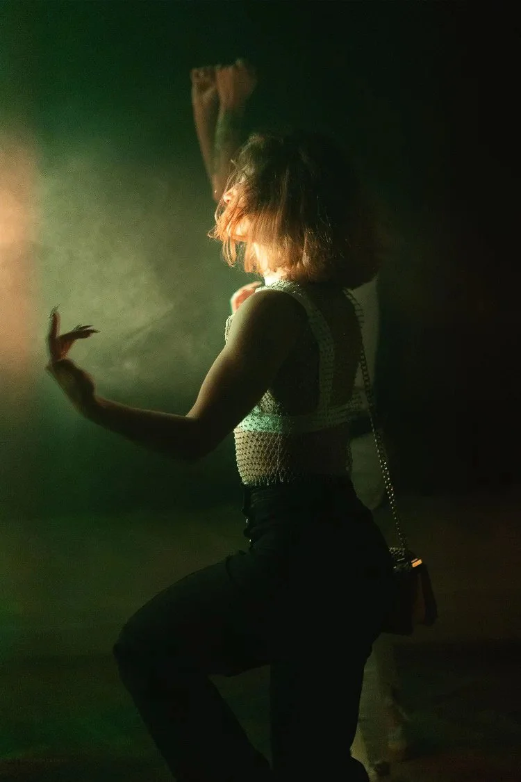 A woman with curly hair dancing in a dimly lit space, illuminated by a soft, warm light.