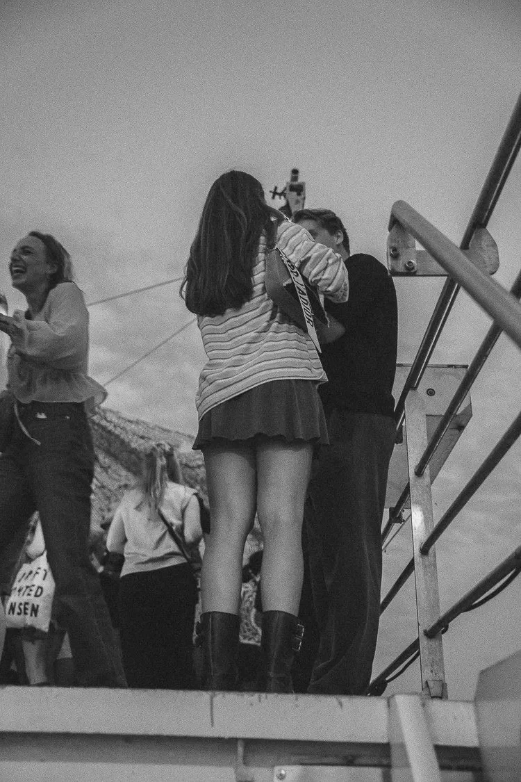 A girl in a striped shirt and skirt hugging a boy on a viewing platform, with a woman laughing nearby and other people in the background.