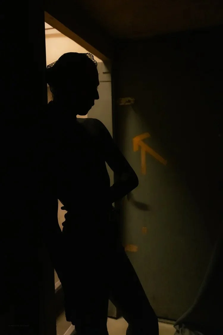 Silhouette of a person standing indoors near a green door with a yellow arrow painted on it, in a dimly lit environment.