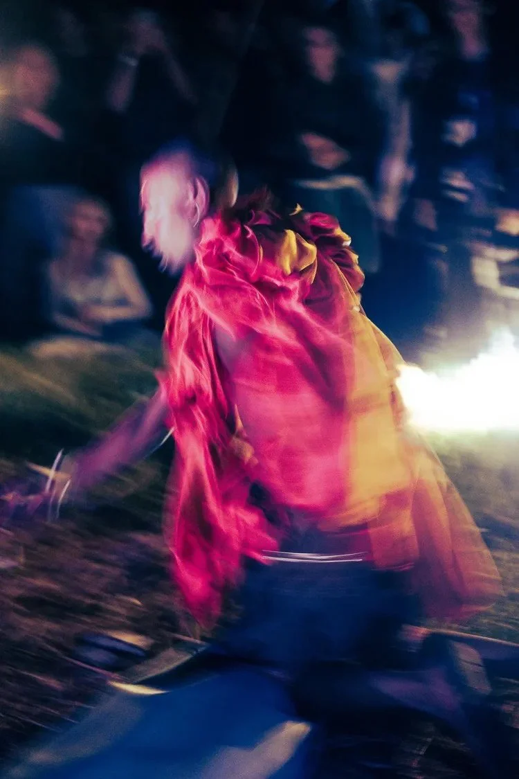 A person in a pink jacket appears to be dancing or moving quickly in a dimly lit environment with blurred motion and indistinct faces of other people in the background.