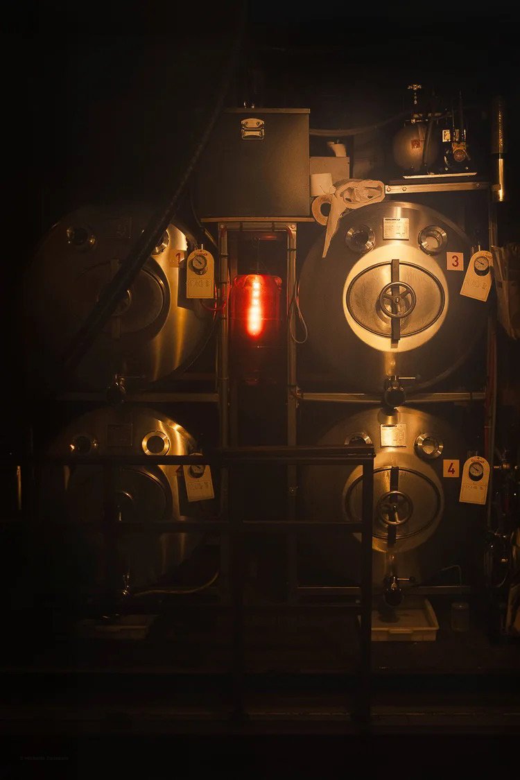 A dark room with industrial equipment, including three large metallic tanks numbered 3 and 4, with a glowing red light in the center and various pipes and gauges.