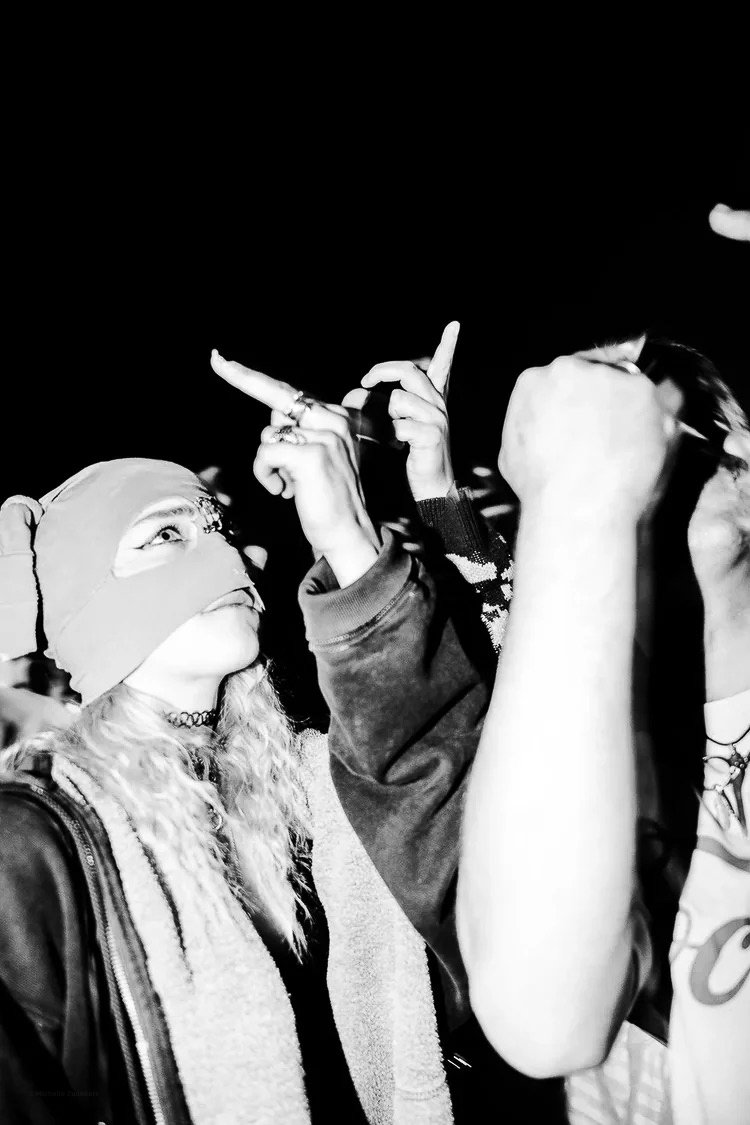 Two people engaged in a protest or confrontation, one with a bandana over their head and the other with their fist raised, during nighttime.