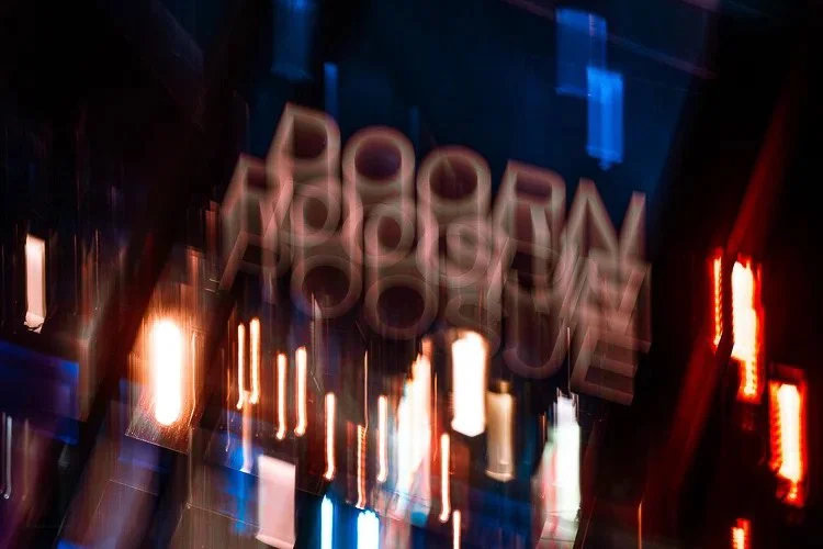 Blurred photo of neon and LED signs with the word 'POOPEN' reflected, in dark ambiance with streaks of red, orange, blue, and white lights.