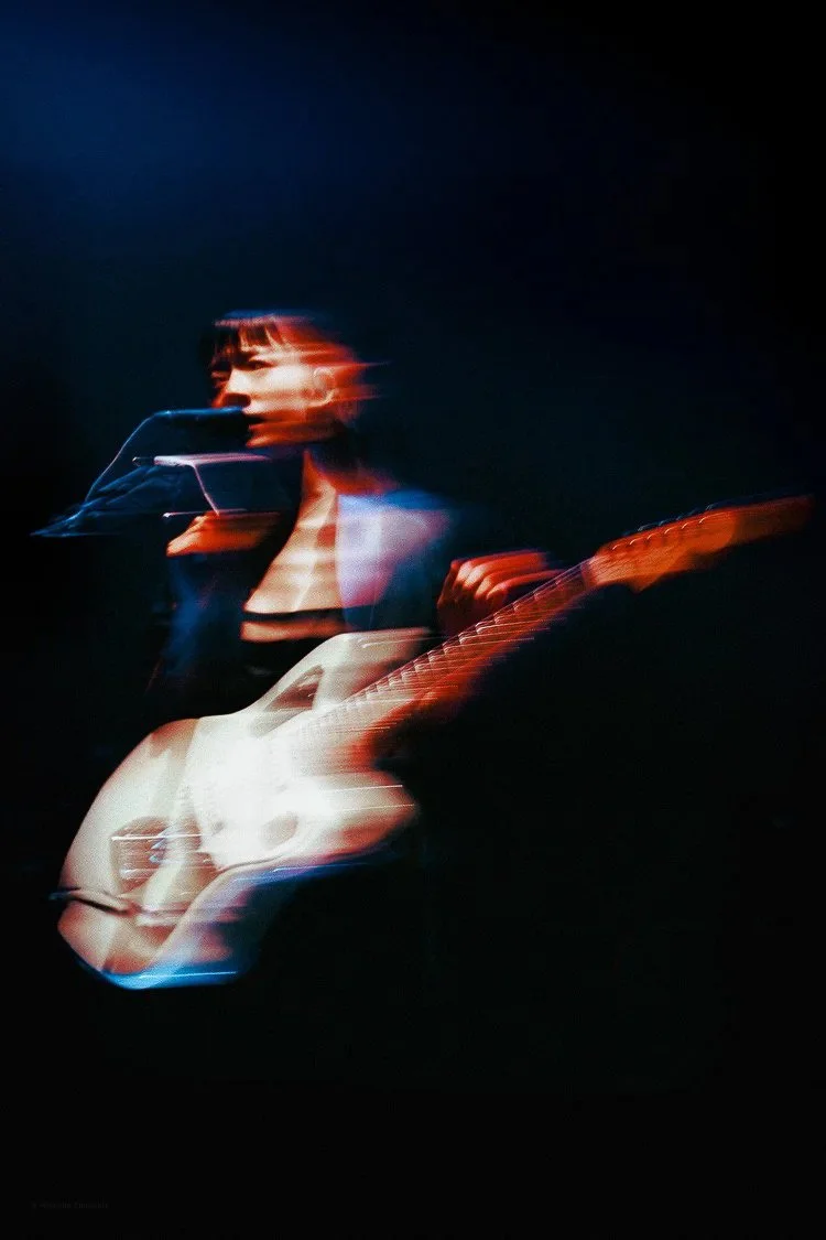 A woman is playing an acoustic guitar in a dark setting with motion blur effects.