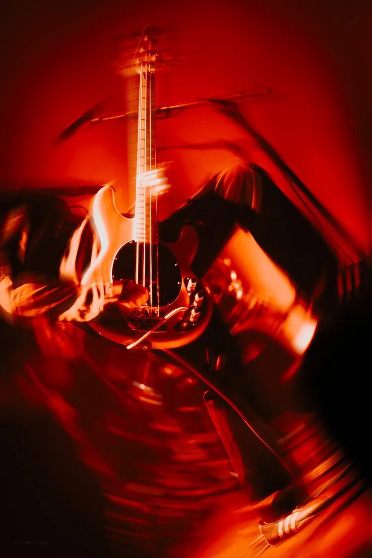 A person playing an electric guitar on stage with dramatic red lighting and motion blur effects.