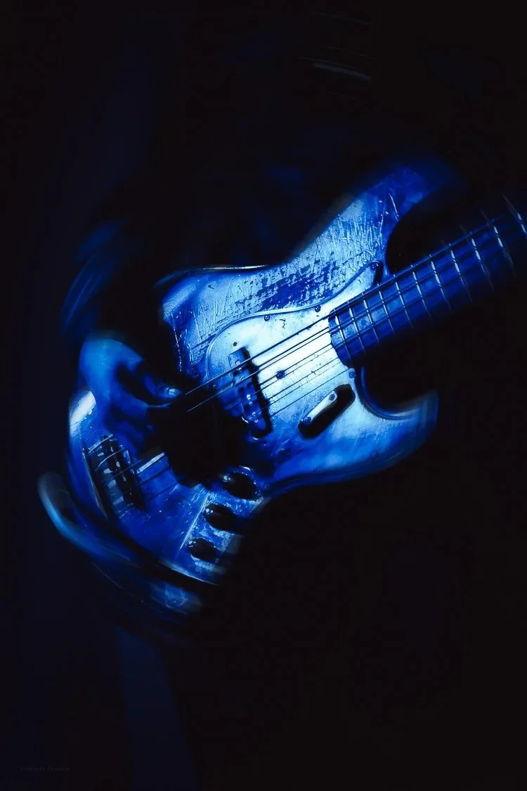 Electric guitar illuminated with blue light in a dark setting.