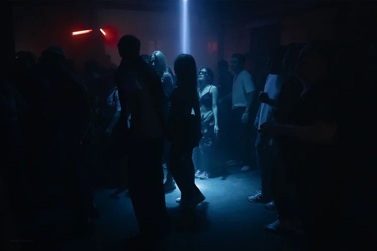 People dancing and socializing in a dimly lit nightclub with blue and red lights.
