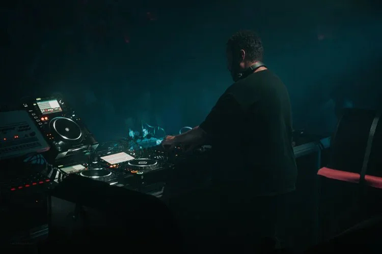 DJ performing at a nightclub with DJ equipment in a dimly lit environment.