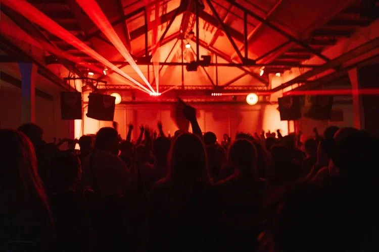 People dancing at a concert or nightclub with red lighting and laser beams.