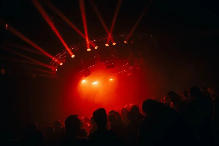 Concert scene with red stage lights illuminating a crowd in a dark venue.