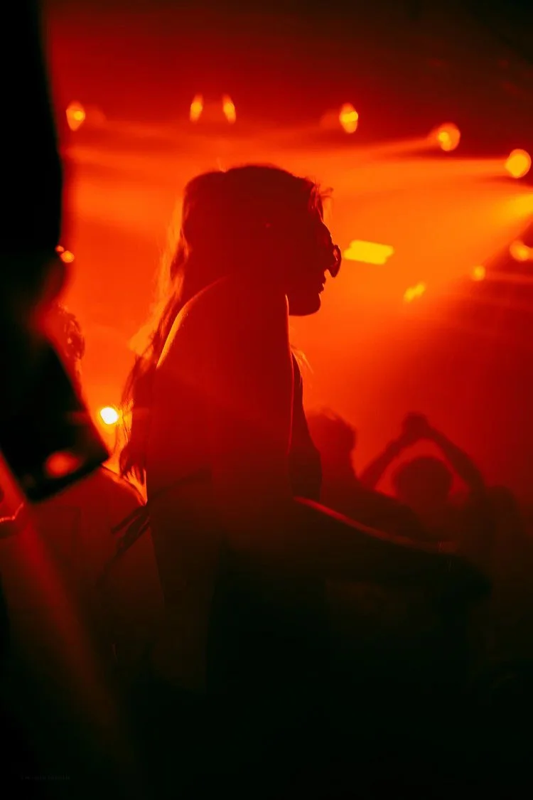 Silhouette of a person with long hair in a dimly lit club with red and orange lighting.