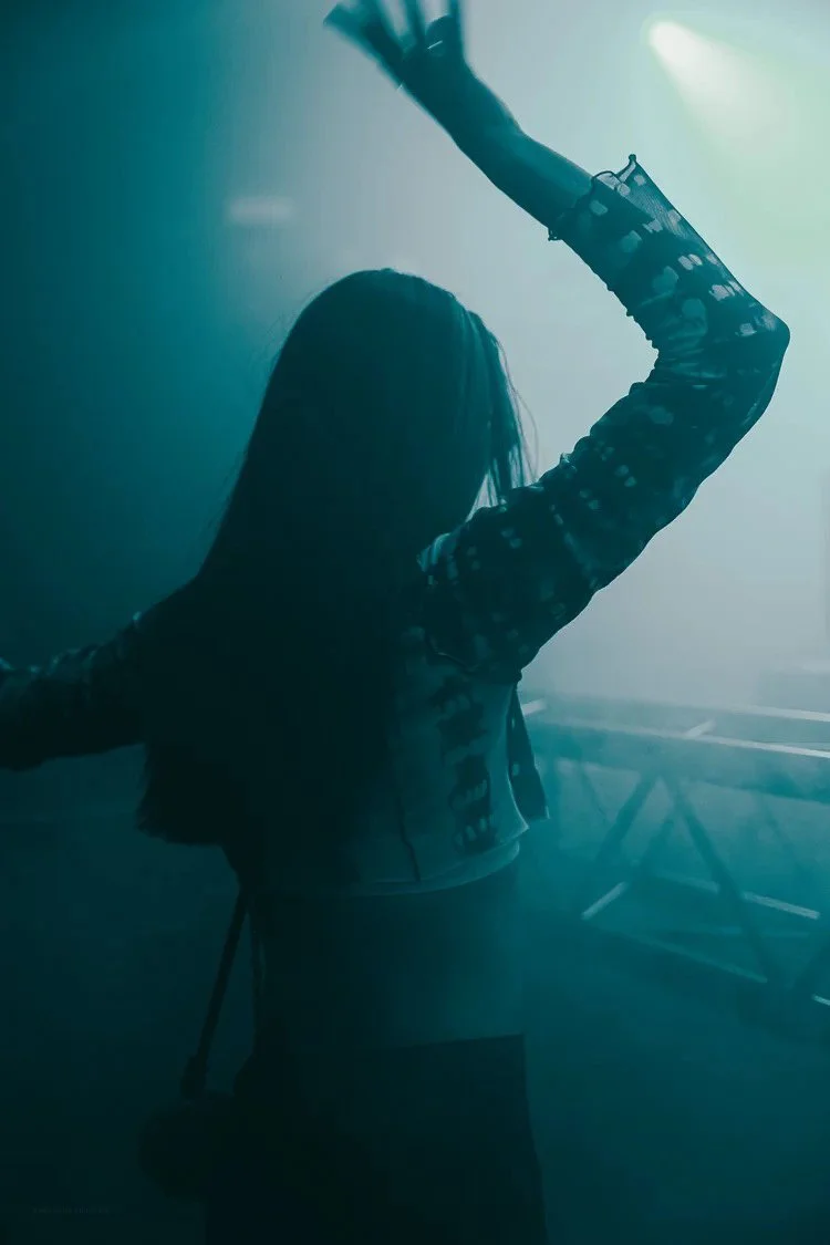 Person dancing or performing on stage in a smoky, blue-lit environment with their arm raised.