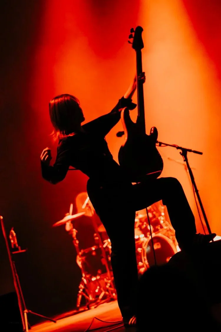 Silhouette of a guitarist with a raised guitar on stage during a concert with warm orange lighting.