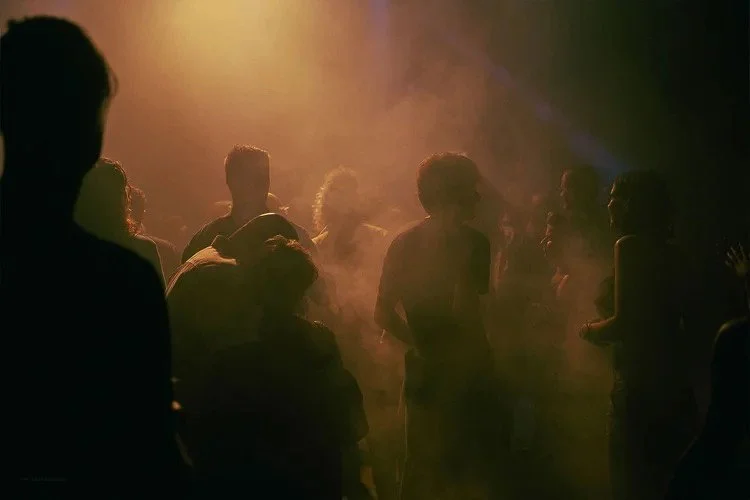 People dancing at a party or nightclub with warm lighting and smoky atmosphere.