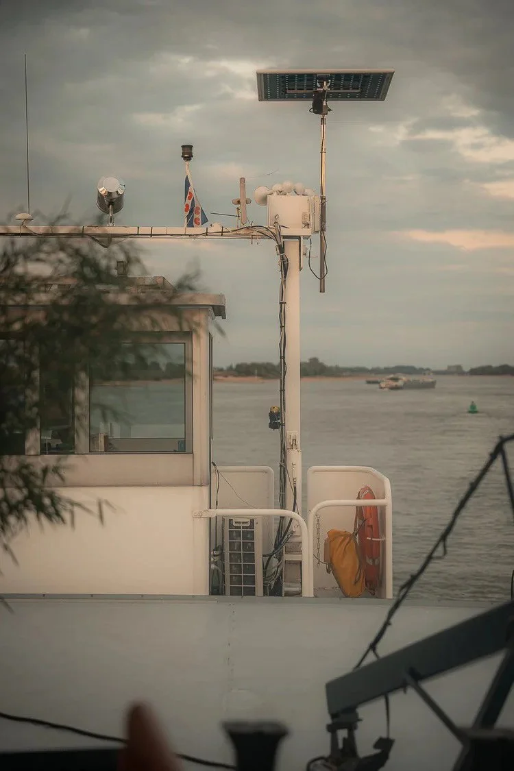 A boat's exterior with a weather station, solar panel, and life preserver, docked by a body of water during overcast weather.