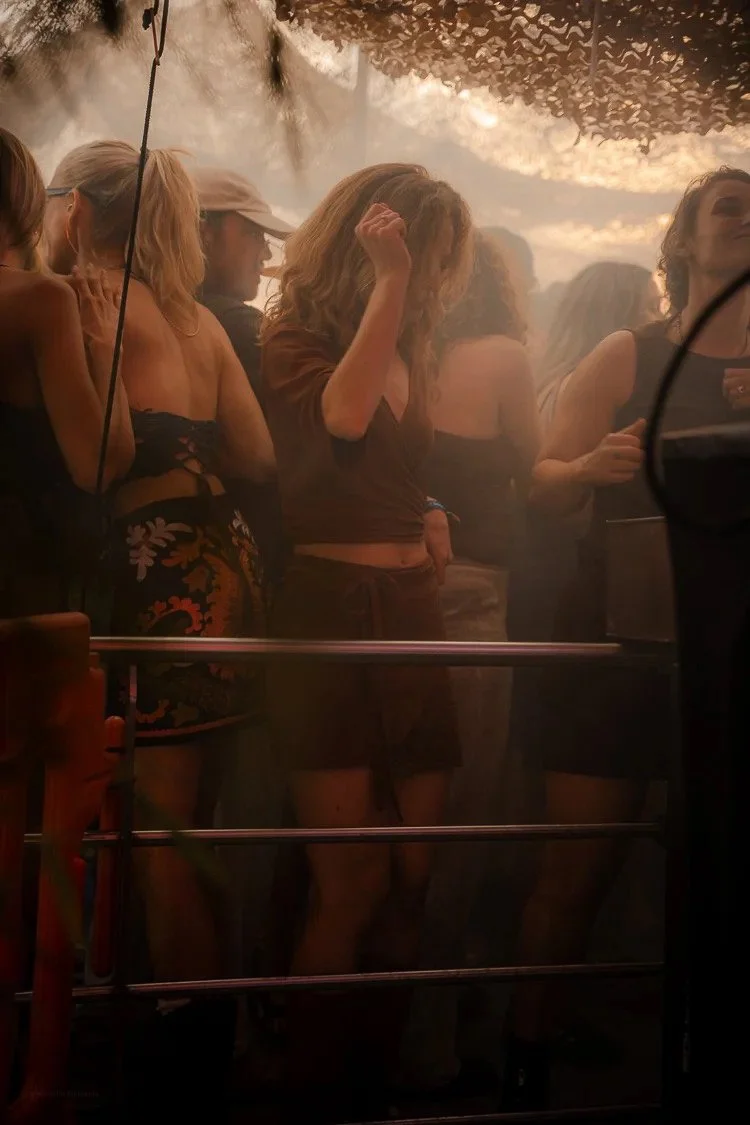 Group of women dancing and enjoying music at a dimly lit concert or party, with a netted ceiling and warm lighting.