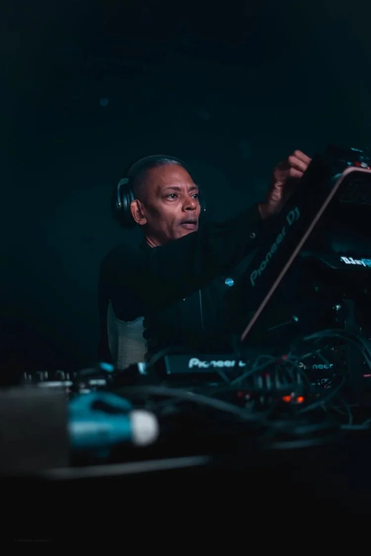 A person wearing headphones DJing with electronic music equipment in a dark setting.