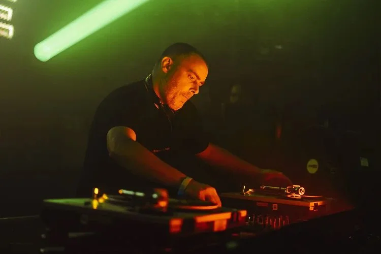 DJ performing at a club with turntables, green laser lights, and dim lighting.