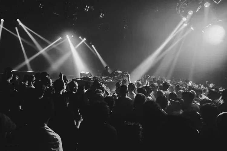 Crowd of people dancing at a nightclub with DJ booth and stage lighting