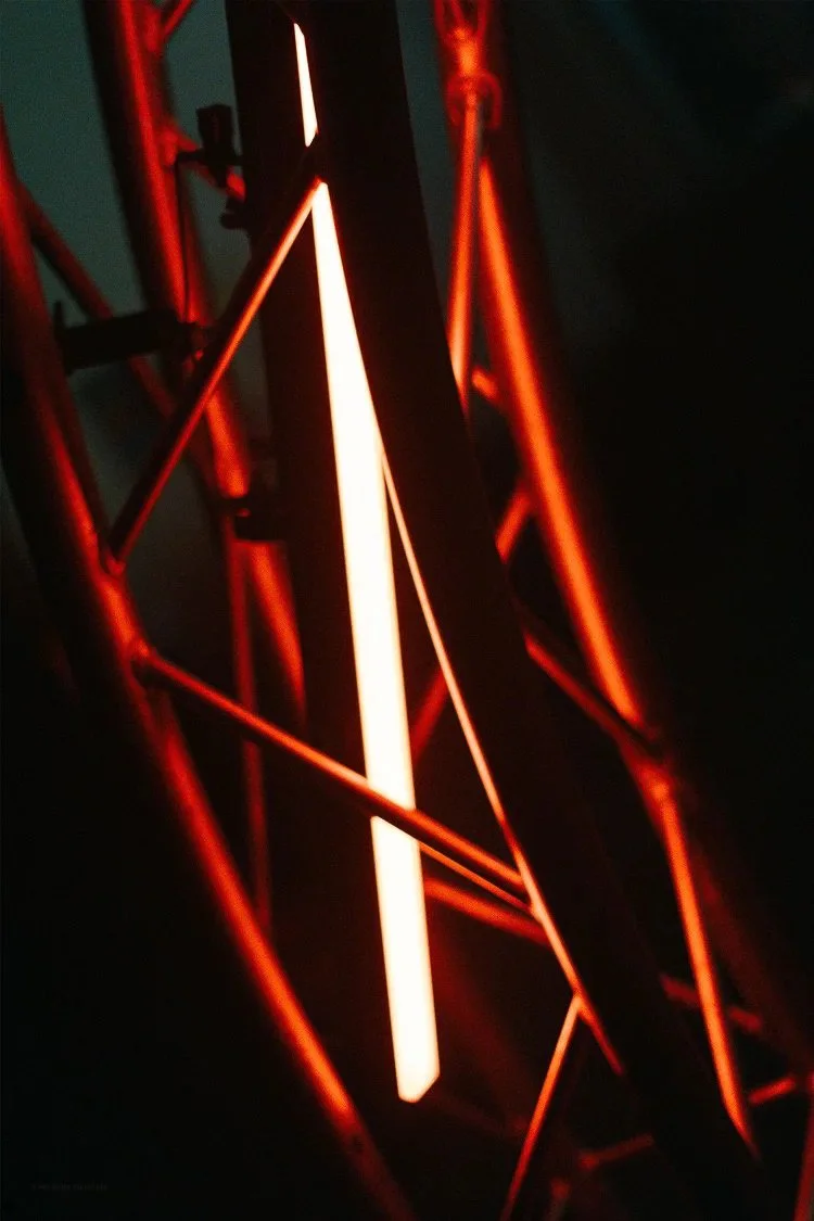 Close-up of illuminated red metal framework with glowing orange and white light strips, possibly part of a modern art installation or architectural structure.