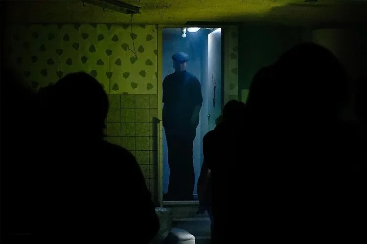 A man standing in a doorway illuminated by blue light, with a group of people in shadow in the foreground.