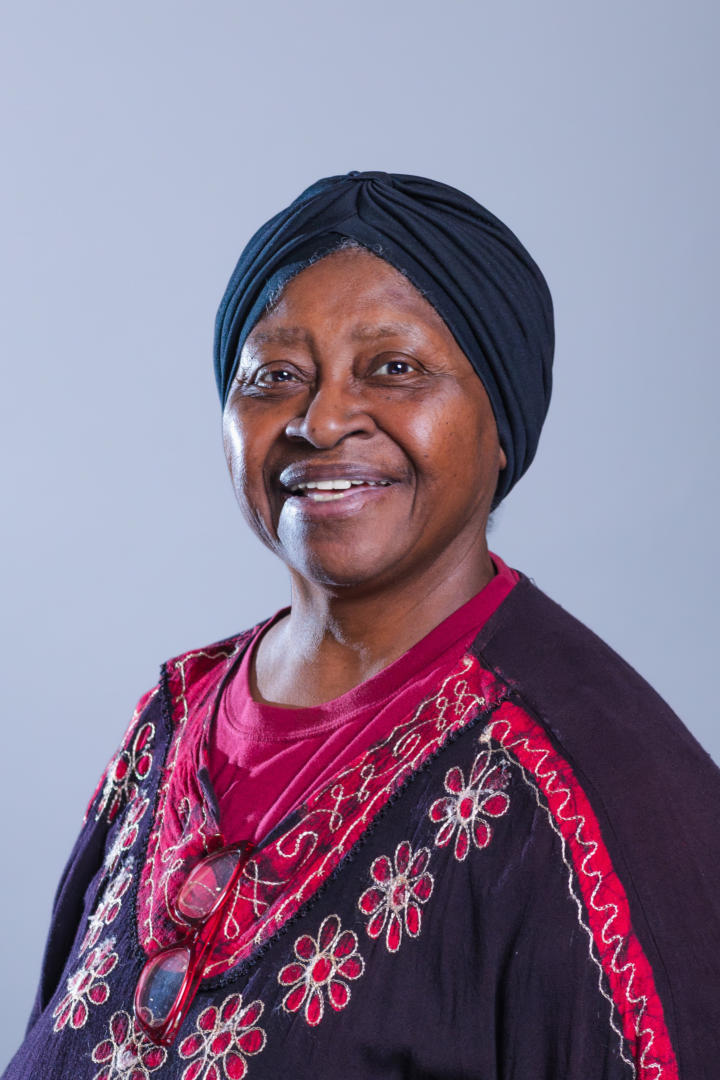 Close-up headshot of Amina Shakir, Member of the NACD Board of Directors, smiling warmly, against a warm grey background.