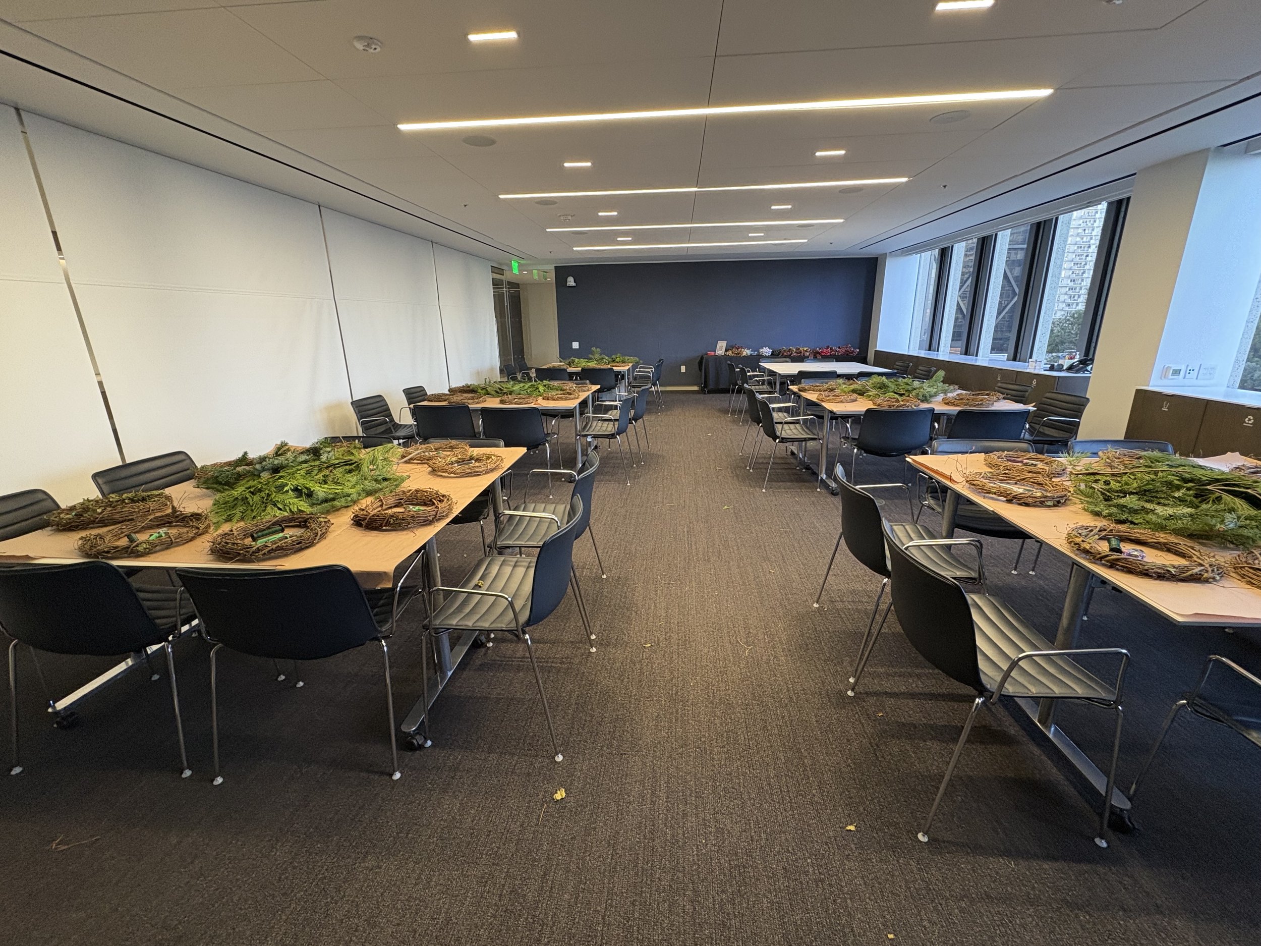 Conference room with tables and chairs, decorated with wreaths and greenery, large windows showing a city view.