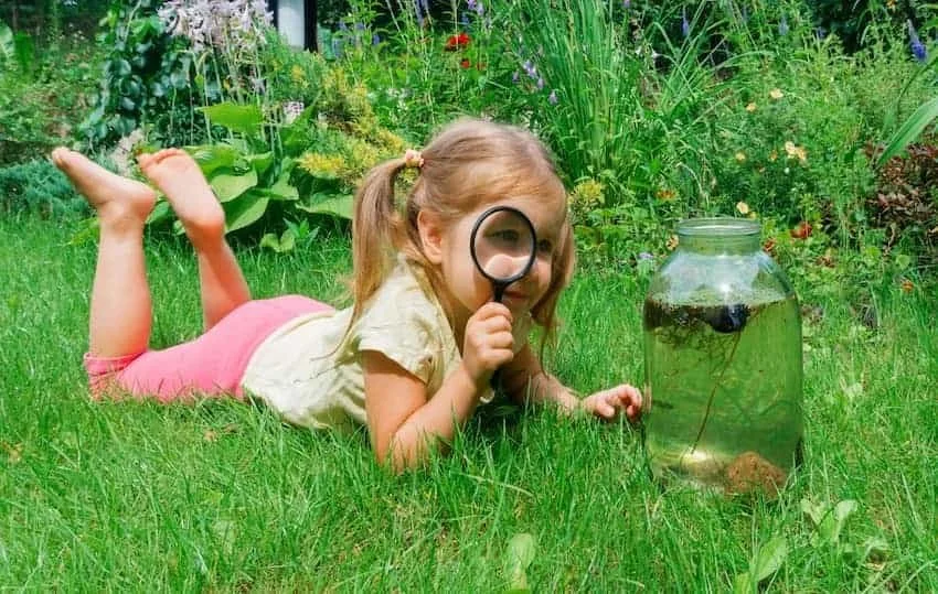 Little girl playing in grass outside with magnifying glass