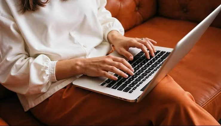 Closeup of woman sitting on couch typing on a laptop
