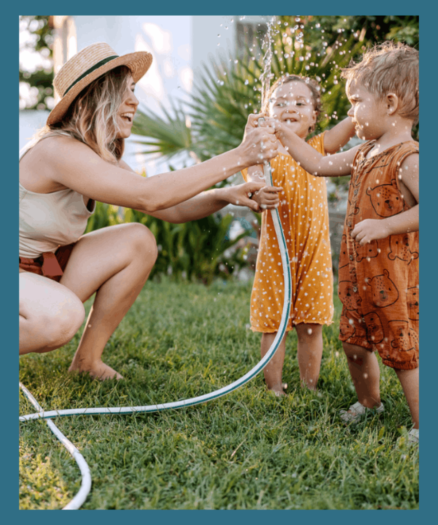 Babysitter is playing outside with two children with a garden hose.
