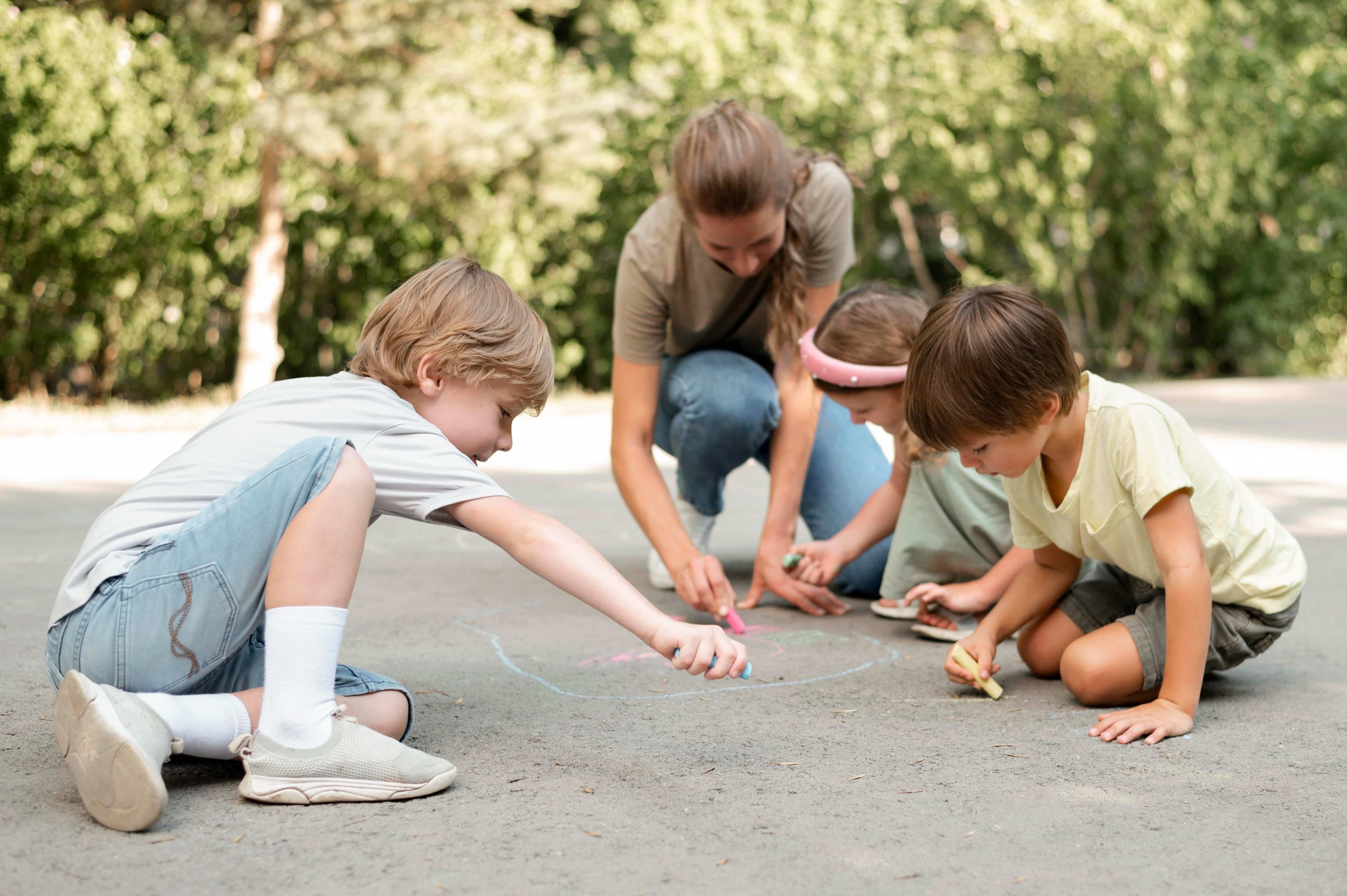 Babysitter playing sidewalk chalk outside with kids.