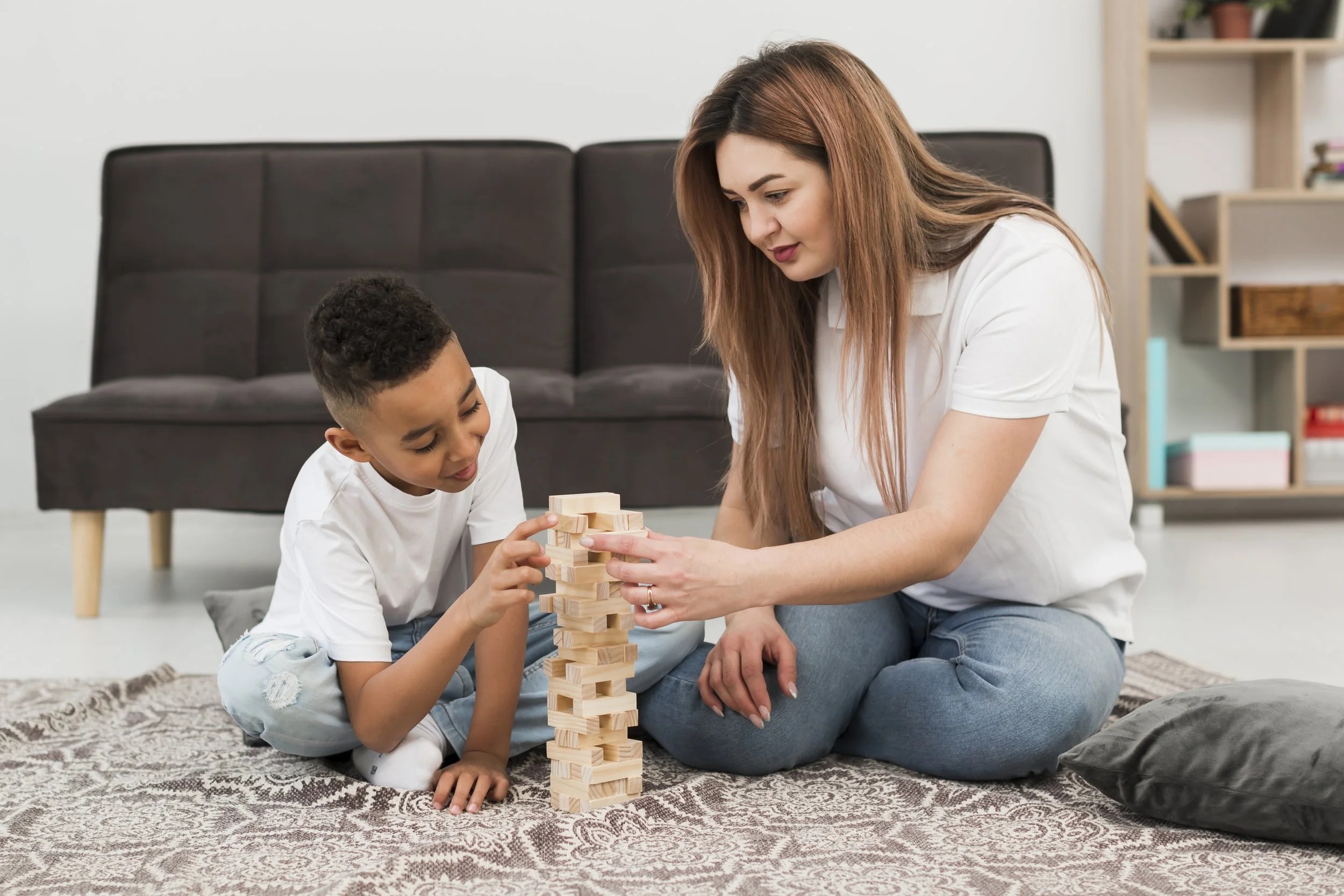 Babysitter and little boy playing Jenga on the floor